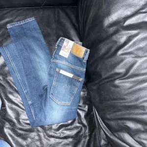 Blåjeans från Nudie - nya - Snygga blå jeans från Nudie Jeans i ekologisk bomull av modell Thin Finn. De har en klassisk femficksdesign med dragkedja och knapp. Perfekta för en stilren look med en bekväm passform. Helt nya! Skinny