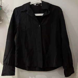 Svart skjorta från & Other Stories - Klassisk svart skjorta från & Other Stories Paris Atelier med lång ärm, knappar framtill och vid manschetten. Skjortan har en rak passform och är tillverkad i 100% silke för en lyxig känsla. Perfekt till jeans eller dressade byxor.