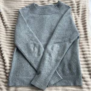 Grå stickad tröja från Vero Moda - Säljer en grå stickad tröja från Vero Moda. Tröjan har en klassisk design med långa ärmar och ribbade muddar vid ärmslut och nederkant. Tröjan är väldigt noppig och är något utsträckt vid kragen, så säljer för billigt pris💗