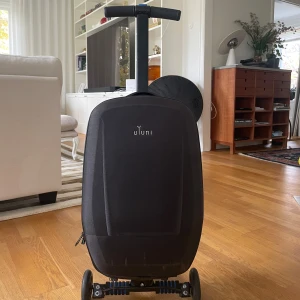 Svart resväska som fungerar som sparkcykel från Uyuni - Cool svart resväska från Uyuni med hårt skal och som fungerar som sparkcykel. Väskan har ett stilrent, modernt utseende och flera praktiska fack på insidan för att organisera dina grejer. Perfekt för dig med barn och som vill resa smidigt! Finns 2x