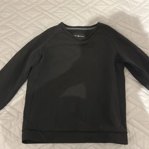 Svart sweatshirt från Sail Racing - Svart långärmad sweatshirt från Sail Racing i storlek small. Tröjan har en stilren design med rund hals och diskreta sömdetaljer på ryggen. Materialet känns mjukt och har en sportig vibe, perfekt för chill dagar. Logga på ärmen och bak i nacken.