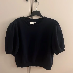 Svart puffärm tröja från Gina Tricot - Säljer en svart tröja från Gina Tricot med puffiga korta ärmar och rund hals. Modellen är croppad och har en stilren look som passar perfekt till jeans eller kjol. Materialet känns mjukt och bekvämt mot huden. Perfekt för dig som gillar trendiga detaljer.