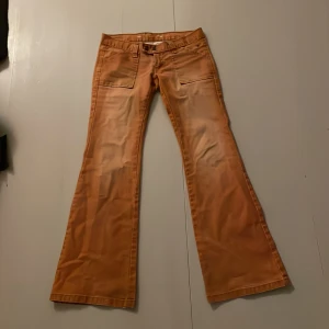 Bootcut jeans från Tommy Hilfiger orange - Snygga orange bootcut jeans från Tommy Hilfiger med låg midja och stora fickor fram. Innebenslängd är 81cm och midjemått, raktöver 39.