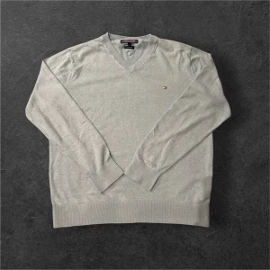 Ljusgrå v-ringad tröja Tommy Hilfiger - Ljusgrå v-ringad tröja från Tommy Hilfiger med diskret logga broderad på bröstet. Tillverkad i en mjuk blandning av bomull och linne, perfekt för lager-på-lager. Långärmad med ribbade muddar och klassisk passform.