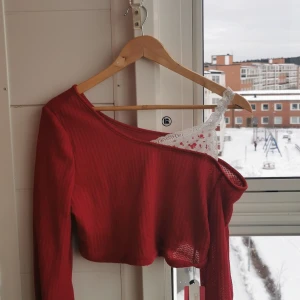Röd croppad oneshoulder topp från Romwe - En oanvänd röd croppad topp från Romwe med oneshoulder-design och lång ärm. Tunt, ribbat material med detail av ett vitt linne med rosor på. 