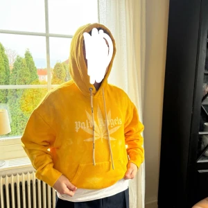 Gul hoodie från Palm Angels - Gul hoodie från Palm Angels med vit logga och stort tryck framtill. Oversized passform, riktigt bra skick näst intill ny!!! Storlek S men passar mig som brukar ha M/L