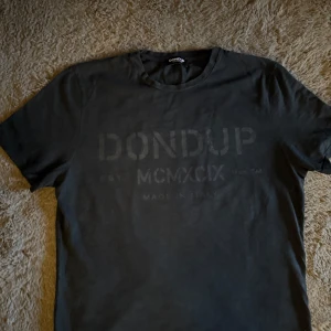 Svart t-shirt från Dondup - Svart t-shirt från Dondup med diskret tryck framtill. Klassisk rund halsringning och korta ärmar. Tillverkad i mjuk bomull för en skön känsla. Snygg och enkel design som passar till allt.