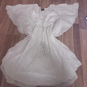 Vit kortklänning från KappAhl S - Superfin vit kortklänning från KappAhl i luftig och lätt bomull. Klänningen har vida fjärilsärmar, snörning med tofs framtill och en flowy passform. Perfekt för varma dagar och ger en riktigt fräsch och somrig vibe.