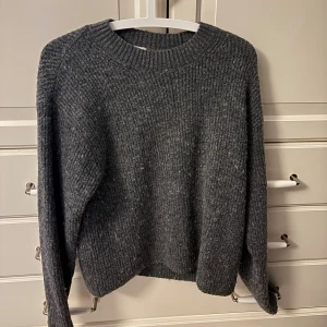 Mörkgrå stickad tröja från H&M - Mysig mörkgrå stickad tröja från H&M med rund halsringning och ribbade muddar. Perfekt för kyliga dagar och enkel att matcha med jeans eller kjol. Klassisk modell med lång ärm och avslappnad passform.