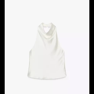 Vit satin linnetopp med halterneck - Säljer en stilren vit linnetopp i satin med halterneck och öppen rygg. Toppen har en mjuk, glansig yta och faller snyggt över kroppen. Perfekt att matcha med jeans eller kjol för en trendig look. Snygg och enkel design utan mönster eller detaljer.