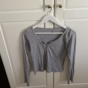 Grå långärmad topp med knappar - Grå långärmad topp från brandy Melville  i mjuk bomullsmix. Toppen har v-ringning med några knappar framtill och en slim passform. Perfekt för en enkel och stilren look. Den är skit snygg och passar till allt. Den köptes för bara någon vecka sedan och kostade 400kr