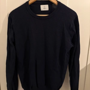 Mörkblå tröja från Bläck - Säljer en mörkblå tröja från Bläck med snyggt strukturerat tyg framtill. Tröjan har rund halsringning och långa ärmar, perfekt för lager-på-lager under kyligare dagar. Enkel och stilren design som funkar till det mesta.