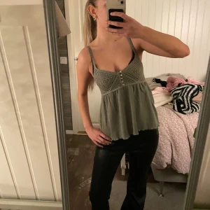 Olivgrön linnetopp med spetsdetaljer - Säljer en olivgrön linnetopp med smala axelband och dekorativa spetsdetaljer upptill. Toppen har små knappar framtill och ett luftigt, lätt rynkat tyg nedtill som ger en flowy känsla. Perfekt för varma dagar och enkel att styla med jeans eller kjol. Köpt i Grekland i somras men aldrig använd!