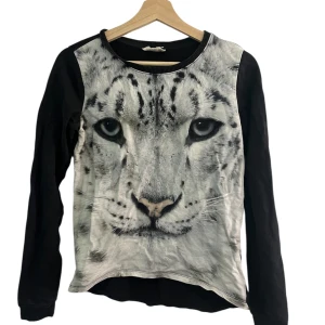 Svart långärmad tröja med leopardtryck - Cool svart långärmad tröja med ett stort tryck av ett leopardansikte på framsidan. Tröjan har rund halsringning och är tillverkad i mjuk bomull.