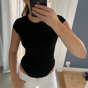 Svart tight topp med dragkedja - Säljer en svart kortärmad body ifrån hm i storlek XS. Bodyn är i ett väldigt bra kvalitet med en dragkedja i ryggen 