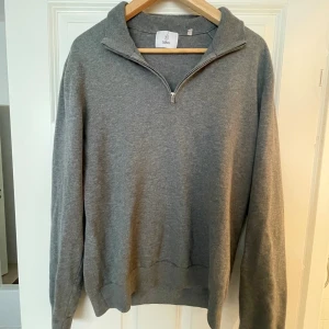 Grå half zip tröja från Bläck - Snygg grå långärmad tröja från Bläck med half zip-dragkedja och hög krage. Tröjan är i mjuk bomullsblandning och har en clean, stilren look som passar perfekt till jeans eller chinos.