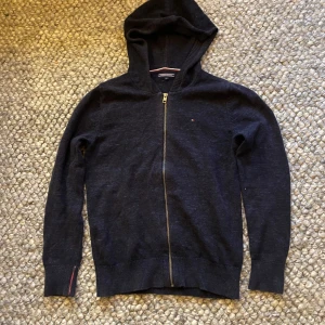 Tommy Hilfiger stickad hoodie - Säljer en stilren mörkblå hoodie från Tommy Hilfiger med dragkedja framtill. Tröjan har långa ärmar och en klassisk huva. Stickad och väldigt skön. Den är i storlek 164 eller XS. Ifall mer frågor eller bilder skriv gärna! Mvh