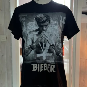 Svart Purpose Tour t-shirt Bieber - Svart t-shirt med stort tryck av Justin Bieber på framsidan och Purpose Tour-tryck på ryggen. T-shirten har rund hals och korta ärmar. Materialet är mjuk bomull, perfekt för dig som gillar bandmerch och streetstyle.