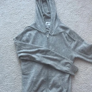 Grå hoodie med dragkedja från John Henric - ❗️pris kan diskuteras❗️Säljer en stilren grå kashmir hoodie från John Henric med dragkedja framtill och huva med snören. Tröjan har två fickor och är tillverkad i mjuk kashmir. Perfekt för dig när du vill ha en enkel och clean look. Fråga för fler bilder!