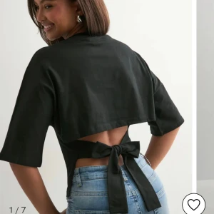 Svart omlottopp med knyt i ryggen - Snygg svart omlottopp med halvlånga ärmar och öppen rygg som knyts med en stor rosett baktill. Toppen har en croppad passform och är tillverkad i ett mjukt bomullsmaterial. Perfekt för dig som gillar trendiga detaljer och vill sticka ut lite extra.