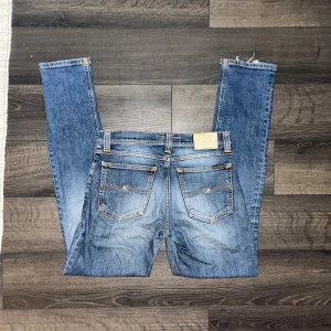 Nudie jeans  - Säljer ett par Nudie jeans i klassisk blå tvätt och kontrastsömmar. Modellen har slim fit, fem fickor och normal midja. Modell Tube Kelly. Midja 37cm, längd 101cm. JAG SKICKAR EJ FLER BILDER NÄR JAG BÄR JEANSEN! för storleksguide hänvisar jag till måtten och för bättre inblick i passformen rekommenderar jag att googla på modellnamnet. Jeansen kan vara uppsydda utan att jag noterat det så kolla måtten noggrant :) s3
