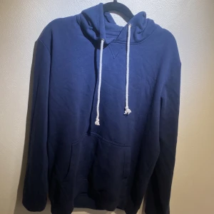 Mörkblå hoodie från Pier One - Mörkblå hoodie från Pier One med vit snörning i huvan och klassisk känguruficka framtill. Tröjan har lång ärm och är tillverkad i mjuk bomull, perfekt för en chill och avslappnad stil.