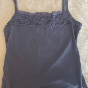 Blå linnetopp med spetskant - Säljer en stilren blå linnetopp med smala axelband och en snygg spetskant upptill. Toppen har en enkel och mjuk design som gör den lätt att matcha med olika outfits. Perfekt för dig som gillar en feminin touch med spetsdetaljer.