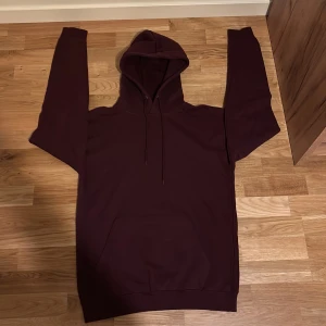 Vinröd hoodie från Studio Total - Säljer en vinröd hoodie från Studio Total i storlek S. Tröjan har huva med snörning och en stor magficka framtill. Perfekt för dig som gillar en enkel och stilren look. Materialet är mjukt och skönt, troligtvis bomull eller bomullsblandning.