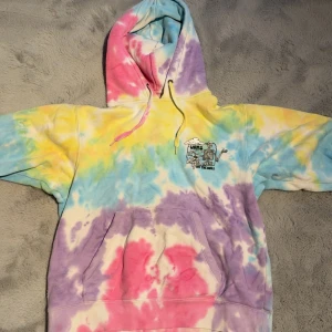 Färgglad tie-dye hoodie från Vans - Säljer en riktigt fet hoodie från Vans med tie-dye mönster i pastellfärger som rosa, gul, blå och lila. Tröjan har huva med snörning, stor magficka och långärmade muddar. Perfekt för dig som gillar streetwear och vill sticka ut med färg.