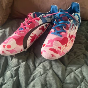 Adidas F50 fotbollsskor camo rosa/blå - ÄNVÄNT BARA I 5-6 träningar.Unika Adidas F50 fotbollsskor med färgstarkt camo-mönster i rosa, blått och vitt. Ena skon har blå snören, den andra rosa. Snygga detaljer som hjärtformade dobbar och grafiska tryck. Skorna har platt sula och är tillverkade i syntetmaterial för bästa prestanda på planen. 