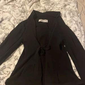 Svart omlottopp från Chiara Forthi XS - Snygg svart omlottopp från Chiara Forthi i storlek XS. Toppen har långa ärmar, djup v-ringning och knyt framtill för en cool och feminin look. Perfekt att styla med jeans eller kjol för en trendig outfit.