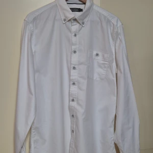 Vit skjorta från Dressmann L - Klassisk vit skjorta från Dressmann med lång ärm, bröstficka och knappar hela vägen framtill. Skjortan har en rak passform och är tillverkad i mjuk bomull, perfekt för en clean och stilren look.