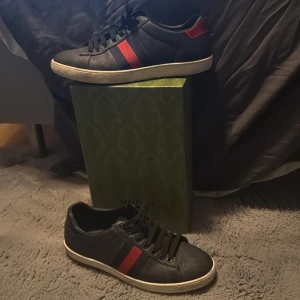 Gucci svarta sneakers med röd/blå detalj - Gucci sneakers i svart skinn med klassiska röd och blå ränder på sidan. Har lite scratches men ändå väldigt bra kondition och väl omhändertagna. Inget kvitto finns men dustbag och shoebox finns.😃