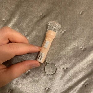 Mini LED ficklampa nyckelring - Smidig och kompakt LED-ficklampa med nyckelring, perfekt att ha med sig i fickan eller väskan. Ger starkt vitt ljus och har enkel av/på-knapp. Produkten är i gott skick utan synligt slitage och fungerar utmärkt enligt bild.