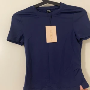 Mörkblå topp från SHEIN - En stilren mörkblå topp från SHEIN med rund halsringning och korta ärmar. Toppen har en slim passform och är tillverkad i ett mjukt, stretchigt syntetmaterial som sitter snyggt på kroppen. Perfekt för dig som gillar enkel och clean stil.