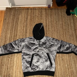 Grå och svart hoodie från Jordan - Säljer en fet hoodie från Jordan 23 Engineered med grått och svart bergsmönster. Tröjan har svart huva med snörning, stor magficka och coolt tryck på bröstet. Perfekt för dig som gillar streetwear och vill sticka ut med en unik design. Nypris 1650 Passar M S o lite tajt på L