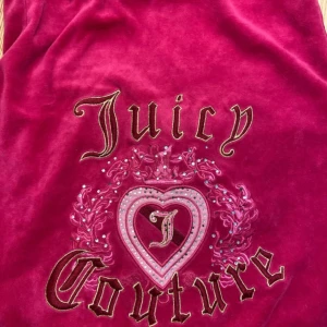 Juicy Couture  - Juicy Couture hoodie i starkt rosa velour med huva och dragkedja. Är i storlek M men känns som S.  Ikoniskt broderi och strassdetaljer på ryggen med hjärta och logga. Mjuk känsla, känguruficka framtill och klassisk passform. Perfekt för dig som vill ha en 00-talsvibe. 