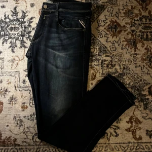 Replay Hyperflex Anbass jeans mörkblå - Snygga Replay Hyperflex Anbass jeans i mörkblå tvätt med diskreta slitningar och kontrastsömmar. Klassisk femficksmodell med Replay-logga på myntfickan. Stretchigt material för extra komfort och smidig passform. Passar typ w32 l32