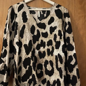 Leopardmönstrad långärmad blus - Säljer en snygg blus från Object med leopardmönster i svart och beige. Blusen har v-ringning och långa ärmar, något kortare framtill. Oanvänd.