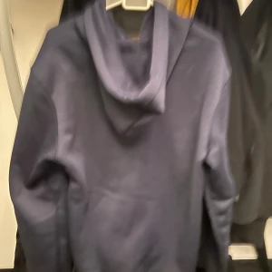 Mörkblå hoodie från polo - Snygg mörkblå hoodie med dragkedja från ralph lauren. Tröjan har huva med snörning, två stora fickor framtill och ett litet broderat ralph lauren på bröstet. Perfekt för chill dagar och enkel att matcha med jeans eller joggers.