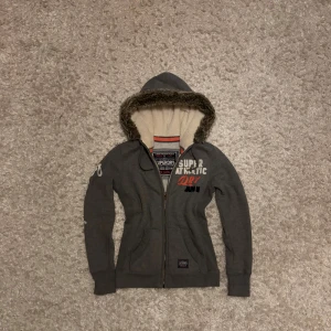 Grå zip hoodie från superdry med päls - Snygg grå hoodie från superdry men fodrad luva och pälskant. Det är en dam modell i storlek S, mycket gott skick. Tveka inte på o skriva vid fler frågor!