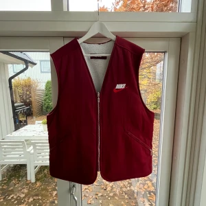 Nike X supreme väst - Nike X Supreme Reversible Nylon Sherpa Vest Burgundy. Storlek M  Axelbredd: 47 cm  Bröst-/vidd (“Width of garment”): 59 cm  Längd: 67 cm  Västen skickas väl förpackad och förseglad i fuktsäker påse, i stabil kartong för säker transport.