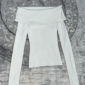 Vit ribbad offshoulder topp - Snygg vit ribbad topp med offshoulder-design och långa ärmar. Den har en bred krage som vilar över axlarna och en tight passform som framhäver siluetten. Perfekt för dig som vill ha en stilren och trendig look. Har haft på mig den bara en gång och priset går o diskuteras 