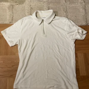 Vit pikétröja med kvartzip från Selected Homme - Säljer en stilren vit pikétröja från Selected Homme i mjuk bomullsfrotté. Tröjan har klassisk krage, korta ärmar och en snygg half zip-dragkedja framtill. Perfekt för en clean och fräsch look.