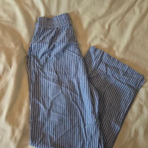 Blåvita randiga byxor från Pigalle - Säljer ett par blå byxor med vita vertikala ränder från Pigalle. Byxorna har resår i midjan och raka ben.. Kan användas som pyjamasbyxor mm. Säljer då de är korta för mig som är 174 lång. Använda ca 2 gånger. Lite skrynkliga då de legat vikta länge