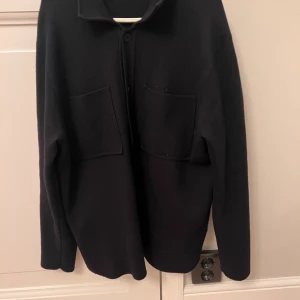 Svart overshirt från Massimo Dutti - Stilren svart overshirt från Massimo Dutti med två stora bröstfickor och klassisk krage. Skjortan har knäppning framtill och är tillverkad i ett mjukt ullmaterial. Har använt den max 5 ggr. Denna Massimo dutti cardigan säljs inte längre, vilket gör den till limited edition. Den är i strl S. Skriv ifall ni har några frågor.