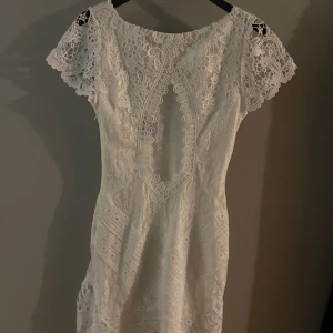 Vit spetsklänning från DRY LAKE med öppen rygg💗  - Lyxig vit spetsklänning från DRY LAKE. Klänningen är figursydd med korta ärmar och en öppen rygg. Perfekt till studenten och midsommar. 💕Skriv för fler bilder