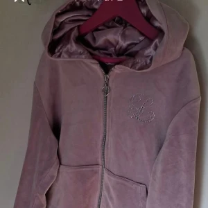 Ljuslila velour hoodie strassdetalj och byxor - Mysig ljuslila hoodie i mjuk velour med dragkedja och huva. Framtill finns en strassdekorerad bokstav och praktisk ficka. Tröjan har snörning nedtill och långa ärmar, perfekt för chill dagar.