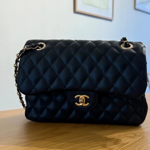 Svart axelväska  - Säljer en ikonisk svart axelväska med guldfärgade detaljer. Väskan har det välkända CC-spännet framtill och vinrött foder med broderad logga. Perfekt för dig som vill ha en tidlös och lyxig accessoar. Använd vid ett tillfälle, så nyskick och väl omhändertagen! 🩷