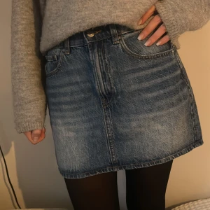 Blå jeanskjol från C Denim, stl S - Snygg blå jeanskjol från C Denim i klassisk femficksmodell. Kjolen är kort och har en rak passform med knapp och dragkedja framtill. Tillverkad i slitstarkt denimtyg med snygga tvättade detaljer. Perfekt att styla med stickad tröja eller t-shirt.